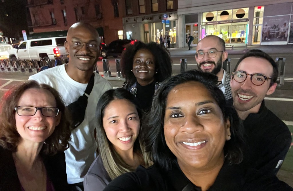 The GitHub staff members who participated in a dinner after their second UNGA event pose for a selfie-style photo on the sidewalk of a city street at night.