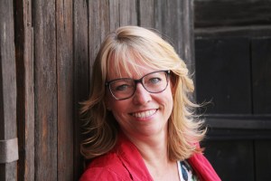 Photograph of Felicitas Heyne, a smiling Caucasian woman with blond hear, wearing dark-framed glasses and a bright red blazer.