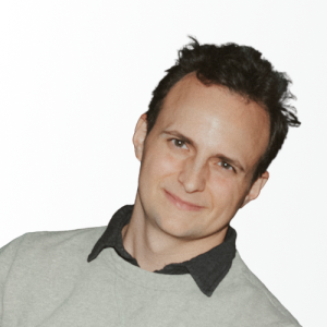 Headshot photograph of Lassor Feasley, a man with short dark hair wearing a tan sweater over a black collared shirt.