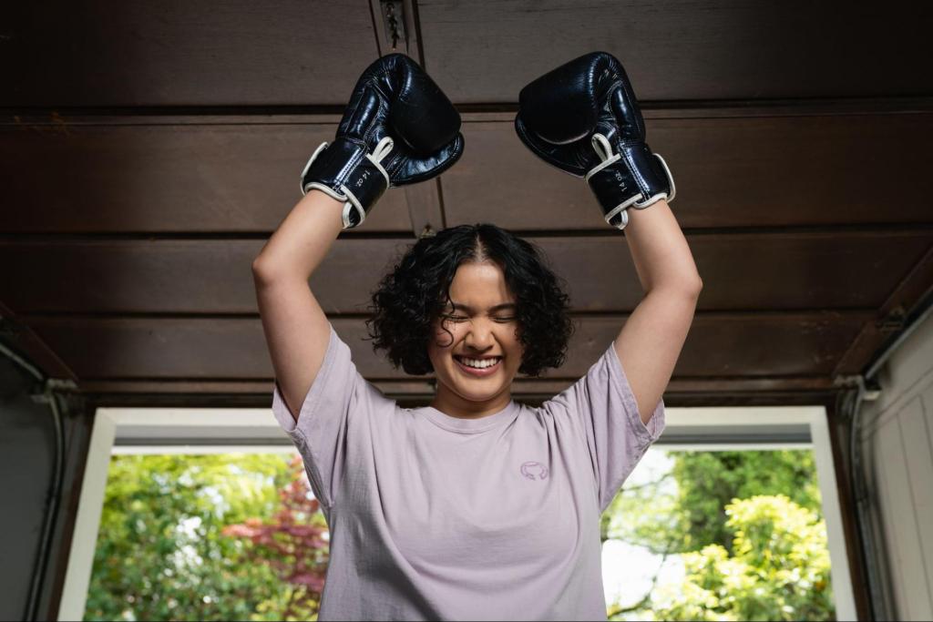 A smiling woman wearing boxing gloves has on a light purple colored t-shirt with a very subtle octocat logo on the left side of the chest area.